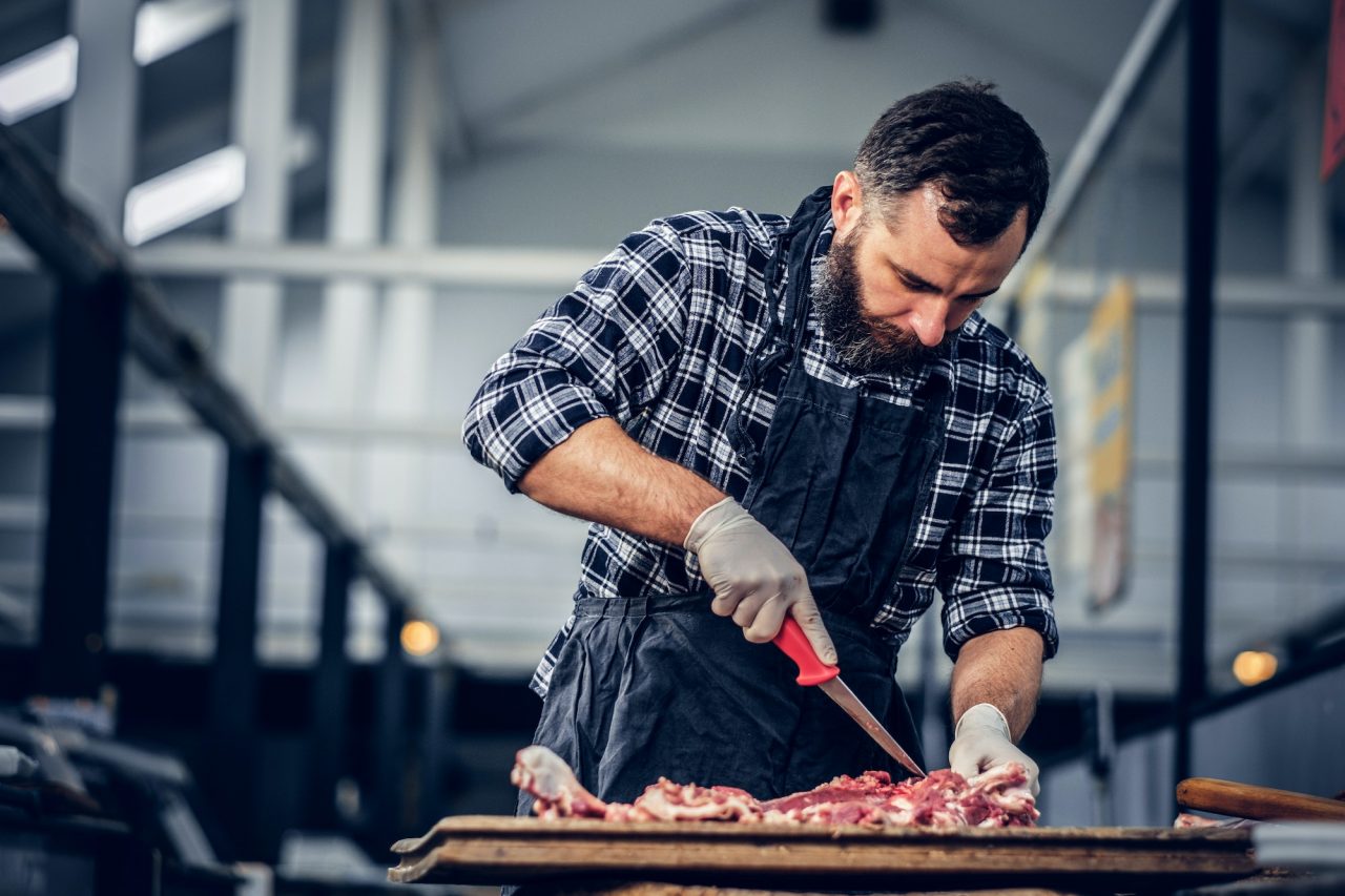Bearded butcher cut fresh bacon meat.